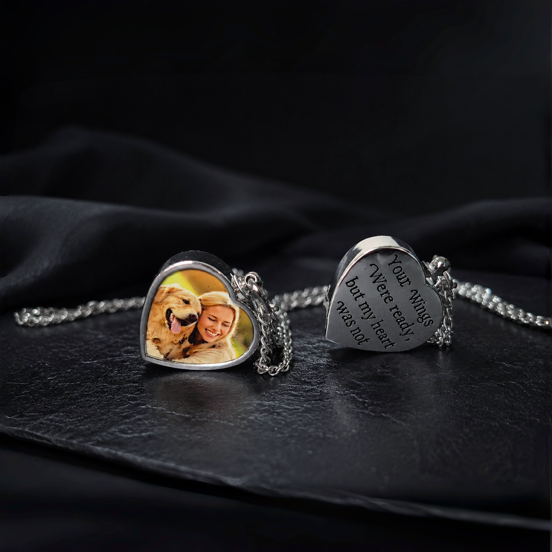 Heart-shaped photo pendant and engraved heart charm on a dark fabric background